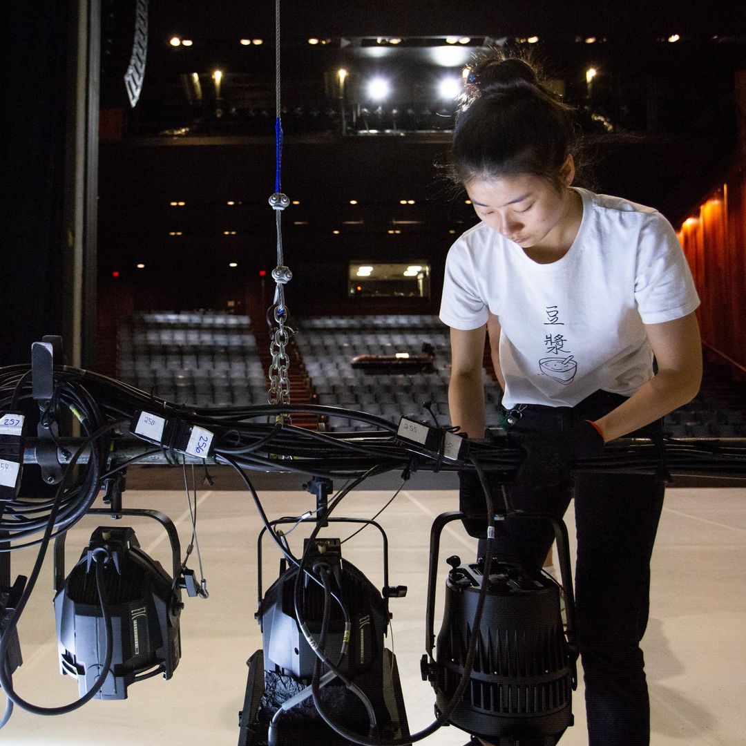 An ADF intern works with a lighting rig on a large stage