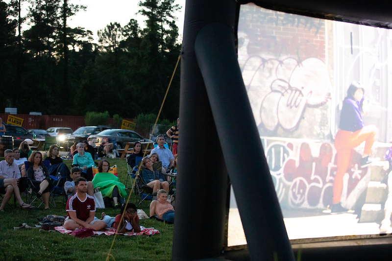 People sitting and watching a dance film on a large screen outdoors
