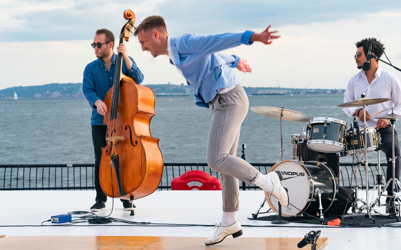 Luke Hickey dancing on an outdoor stage with musicians playing behind him