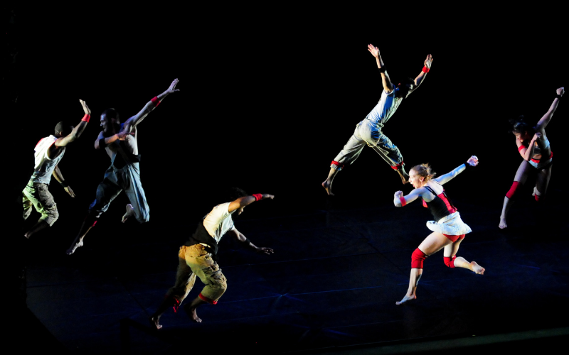 Six dancers doing different movements on a dark stage