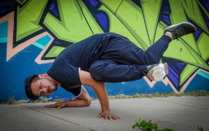 Jose Velasquez break dancing in front of a wall with colorful graffiti