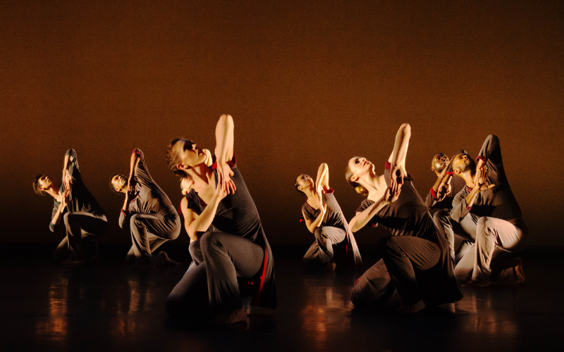 7 dancers on stage posing with their knee on the ground and elbow in the air.