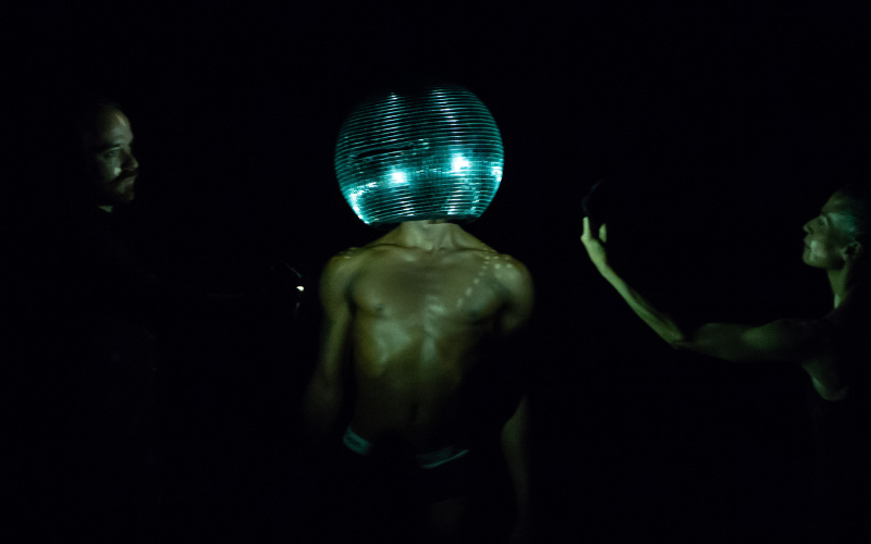 Two people spin a person in the middle with a disco ball over their head